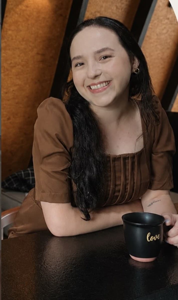 Pietra Malinverno, fisioterapeuta pélvica em Itapema, sorrindo à mesa com uma xícara